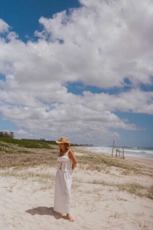 A woman wearing The Desert Cowboy straw fedora hat on a beach with clouds in the sky