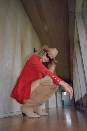 Model wearing a tan Desert Rose straw cowboy hat, red outfit, and sunglasses in a hallway.
