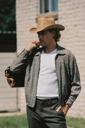 Man wearing a tan straw cowboy hat, holding a bag, outdoors.