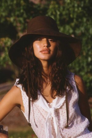 Model wearing a brown cotton bucket hat with a neck tie, outdoors.
