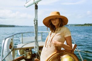 A woman wearing a tan corduroy bucket hat on a boat, with a scenic water background.
