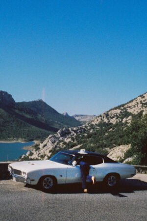 A vintage car parked by a lake with mountains in the background.