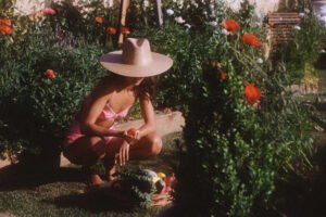 A woman wearing a Palma Wide Fedora in a garden, crouching with a basket of vegetables.