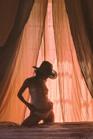 Silhouette of a person wearing a brown straw cowboy hat, with soft light filtering through curtains