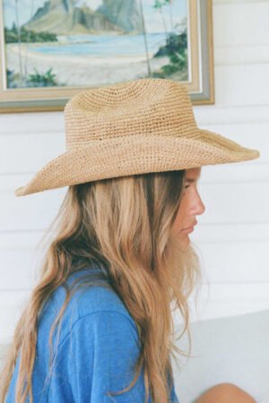Profile view of a woman wearing a natural raffia cowboy hat, showcasing its texture and style.