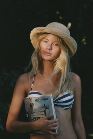 Model wearing Raffia Cruiser straw boater hat, holding a magazine, outdoors