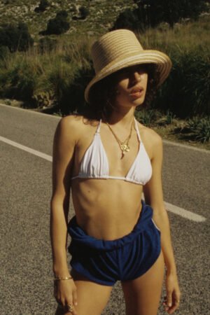 Model wearing the Reef Bucket hat, a straw bucket hat in white, on a sunny road.
