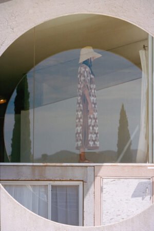 Model wearing The Cove straw bucket hat in natural color, standing in a circular window.
