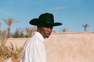 Model wearing The Ridge black wool felt cowboy hat outdoors with palm trees in background