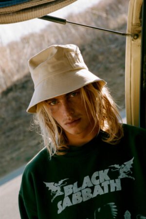 Model wearing a beige cotton bucket hat, with a casual black sweatshirt featuring 'BLACK SABBATH' text.