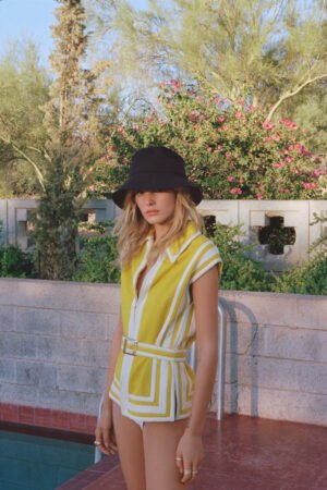 Model wearing a black Wave Bucket Hat by Lack of Color, standing by a pool with greenery in the background.