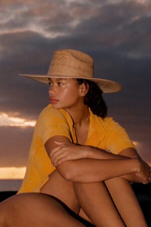 Model wearing a Western Wide Palma straw cowboy hat against a sunset background.