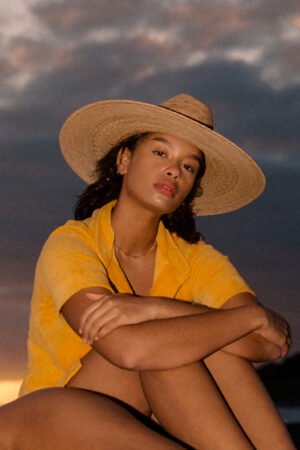 Model wearing a Western Wide Palma straw cowboy hat, sitting outdoors at sunset.